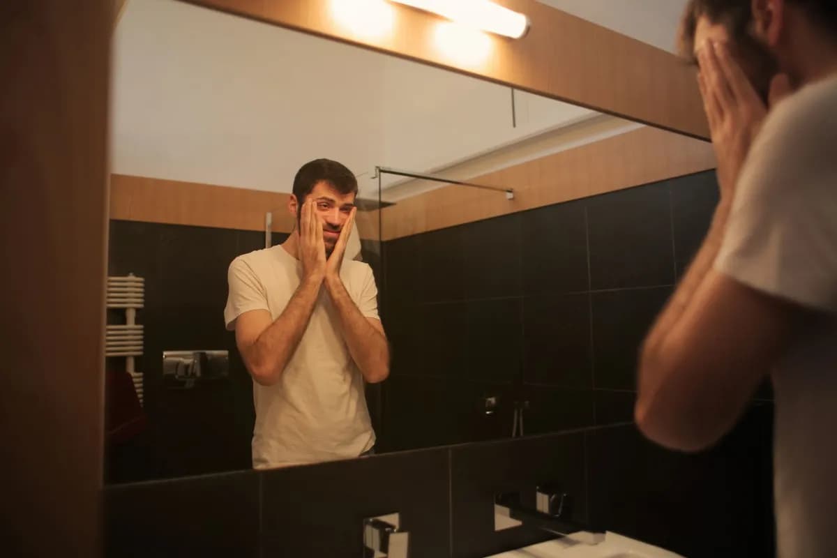 Man examining his hairline in bathroom mirror — recognising early signs of male pattern baldness in Malta