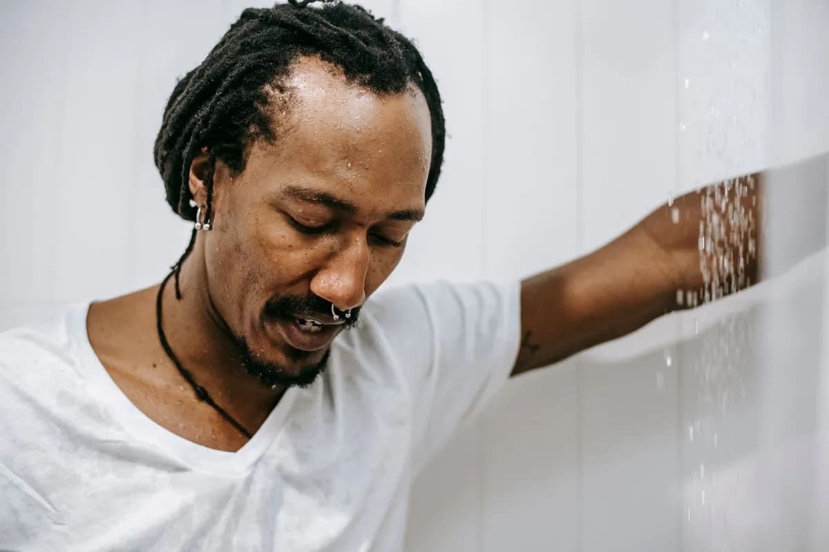 Man in shower looking concerned at hair shedding during topical hair-growth treatment, Malta