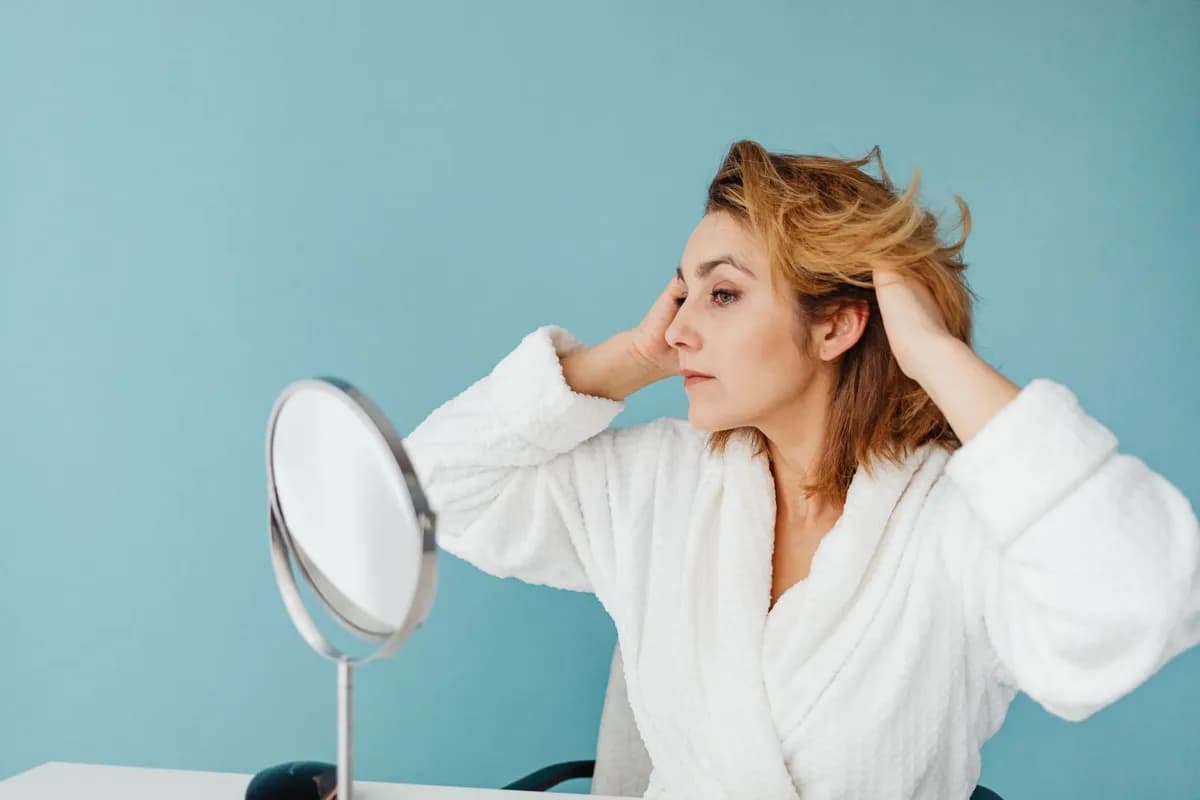 Woman examining her hair in mirror, representing female pattern hair loss and topical hair-growth treatment options in Malta